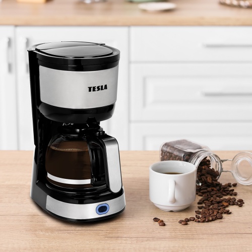 Kávovar TESLA Coffeemaster ES200 v černém provedení na kuchyňské lince s hrnkem a rozsypanými kávovými zrny na boku.